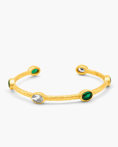 Gold bangle with green and clear gemstones on a white background