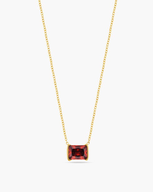 Gold necklace with a red gemstone pendant on a white background