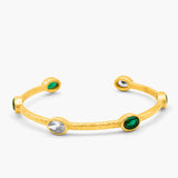 Gold bangle with green and clear gemstones on a white background